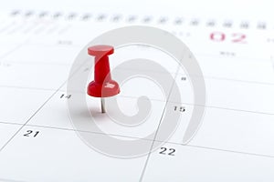 Concept image of a Calendar with red push pin. Closeup shot thumbtack attached. The words heart shape written on white