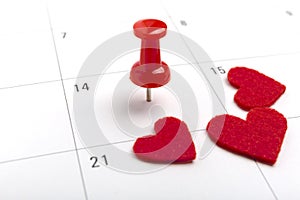 Concept image of a Calendar with red push pin. Closeup shot thumbtack attached. The words heart shape written on