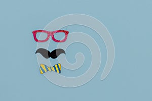 Concept image with glasses, moustache and bow tie on light blue background as resource for creative projects, copy space on the