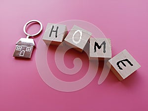 concept image a house key chain and wooden block word - HOME on pink background with selective focus.