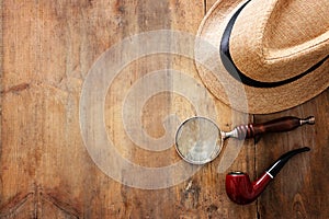 Concept image of investigation or private detective. Fedora hat, magnifing glass and vintage items over wooden table