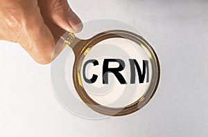 A concept image of a man hand holding magnifying glass with a word CRM zoom inside the glass