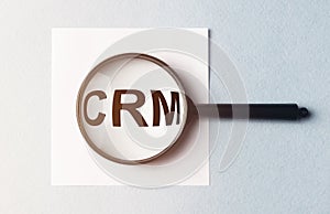 A concept image of a man hand holding magnifying glass with a word CRM zoom inside the glass