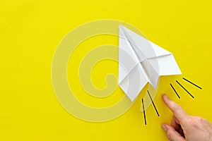 Concept image of person hand directing paper plane over yellow background