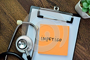 Concept of Impetigo write on sticky notes with stethoscope isolated on Wooden Table