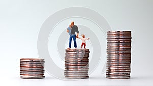 Miniature men and miniature children standing on a pile of coins.