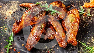 The concept of Indian cuisine. Baked chicken wings and legs in honey mustard sauce. Serving dishes in the restaurant on a black