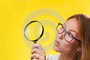 The concept of information retrieval. A blonde woman with glasses, looks in surprise through a magnifying glass. Portrait close up