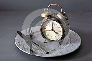 Concept of intermittent fasting, ketogenic diet, weight loss. alarmclock fork and knife on a plate