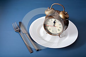 Concept of intermittent fasting, ketogenic diet, weight loss. alarmclock fork and knife on a plate