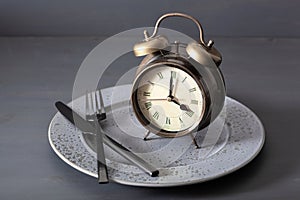 Concept of intermittent fasting, ketogenic diet, weight loss. alarmclock fork and knife on a plate photo