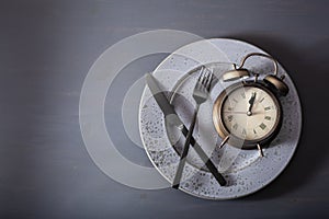 Concept of intermittent fasting, ketogenic diet, weight loss. fork and knife, alarmclock on plate