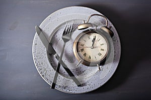 concept of intermittent fasting, ketogenic diet, weight loss. fork and knife, alarmclock on plate