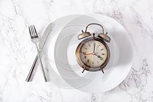 Concept of intermittent fasting, ketogenic diet, weight loss. fork and knife crossed and alarmclock on a plate