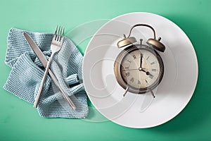 Concept of intermittent fasting, ketogenic diet, weight loss. fork and knife crossed and alarmclock on plate