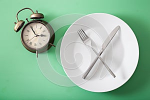 Concept of intermittent fasting, ketogenic diet, weight loss. fork and knife crossed on a plate and alarmclock