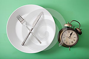 Concept of intermittent fasting, ketogenic diet, weight loss. fork and knife crossed on a plate and alarmclock