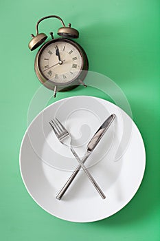 Concept of intermittent fasting, ketogenic diet, weight loss. fork and knife crossed on a plate and alarmclock