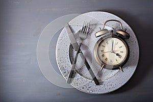 Concept of intermittent fasting, ketogenic diet, weight loss. fork and knife crossed on a plate and alarmclock