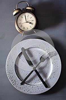 Concept of intermittent fasting, ketogenic diet, weight loss. fork and knife on a plate and alarmclock