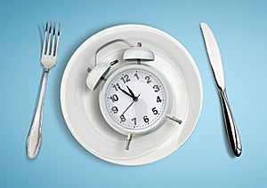 Concept of intermittent fasting, lunchtime, diet and weight loss. Alarm clock on plate