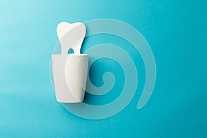 The concept of the International Day of the Dentist. A white cup for toothbrushes and a paper tooth on a blue background