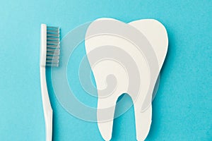 The concept of the International Day of the Dentist. A white toothbrush and a paper tooth on a blue background