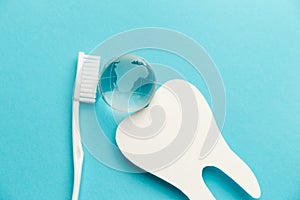 The concept of the International Day of the Dentist. White toothbrush, paper tooth and glass globe on a blue background