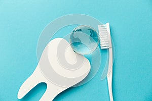 The concept of the International Day of the Dentist. White toothbrush, paper tooth and glass globe on a blue background