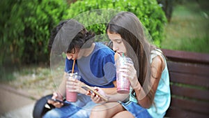 Concept of internet addiction, teen boy and girl use their smartphones, sitting hunched on a bench in the park on a