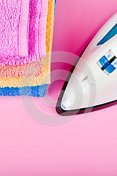 The concept of ironing clothes. House order. Iron and ironed fabric. Electric iron on a pink background with towels. multi-colored