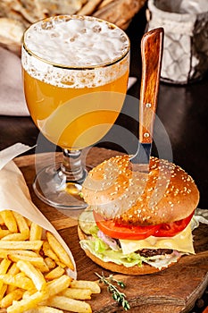 The concept of Italian cuisine. Italian burger with french fries on a wooden board and a glass of light beer with foam