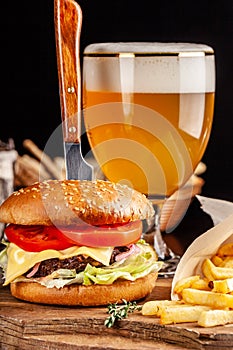 The concept of Italian cuisine. Italian burger with french fries on a wooden board and a glass of light beer with foam