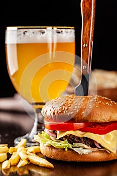 The concept of Italian cuisine. Italian burger with french fries on a wooden board and a glass of light beer with foam