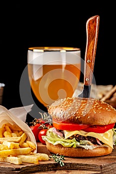 The concept of Italian cuisine. Italian burger with french fries on a wooden board and a glass of light beer with foam