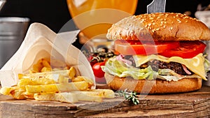 The concept of Italian cuisine. Italian burger with french fries on a wooden board and a glass of light beer with foam