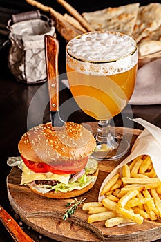 The concept of Italian cuisine. Italian burger with french fries on a wooden board and a glass of light beer with foam