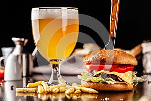 The concept of Italian cuisine. Italian burger with french fries on a wooden board and a glass of light beer with foam. Serving