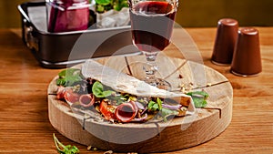 Concept Italian cuisine. Piadina with ham, tomatoes, mix lettuce, pistachios, cucumbers on wooden board. Glass of red wine