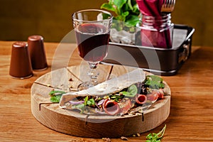 Concept Italian cuisine. Piadina with ham, tomatoes, mix lettuce, pistachios, cucumbers on wooden board. Glass of red wine