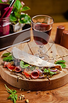 Concept Italian cuisine. Piadina with ham, tomatoes, mix lettuce, pistachios, cucumbers on wooden board. Glass of red wine