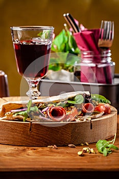 Concept Italian cuisine. Piadina with ham, tomatoes, mix lettuce, pistachios, cucumbers on wooden board. Glass of red wine photo