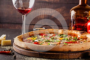 Concept Italian cuisine. A real pizza with vegetables and ham, bacon and parmesan cheese. The ingredients on the table. Red wine