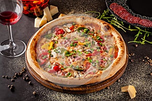 Concept Italian cuisine. A real pizza with vegetables and ham, bacon and parmesan cheese. The ingredients on the table. Red wine