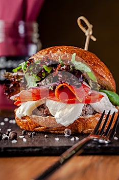 Concept of Italian home cooking. Burger with beef and pork meat cutlet, mozzarella cheese, salami sausage, parma, arugula