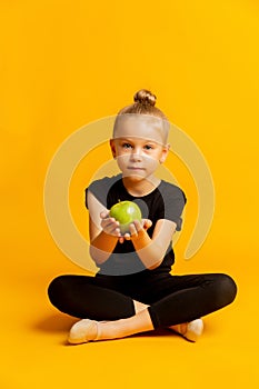 Concept of kid`s sports and healthy eating. Happy cheerful excited confident gymnast girl is holding a green fresh apple