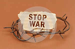 On a brown surface, barbed wire and a cardboard sign with the inscription - Stop war