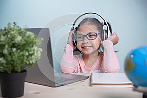 Concept learning online social distance. Asian kids girls wearing glasses, headphones smile happily looking at a laptop. Listen to