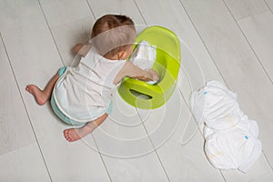 The concept of learning to use the chamber pot. close-up: a little cute baby sits on the floor and plays: puts clean diapers in a