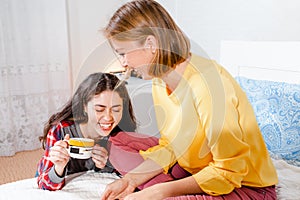 The concept of lesbian relationships. LGBT PERSON. Two young women sit together on the bed, drink drinks and laugh merrily,
